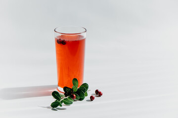 brightly colored lingonberry drink in clear glass features striped straw. fresh lingonberries and green leaves lie beside glass, creating vibrant presentation. close up.