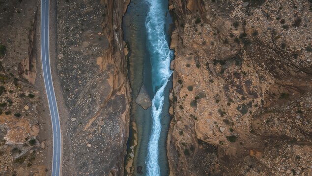 Aerial view of a winding river surrounded by rocky terrain and a narrow road, showcasing contrasting textures