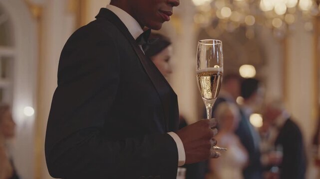 Elegant video scene capturing a close-up, side angle of a person in formal attire holding a champagne glass, with a luxurious, blurred background.