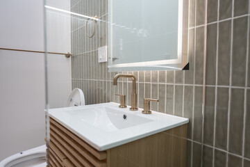 Modern bathroom vanity featuring a white sink, bronze faucet, gray tile backsplash, and illuminated...