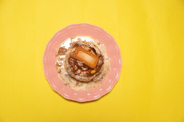 A gourmet cinnamon roll on a pink plate with yellow background