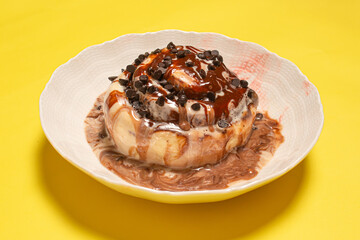 A delicious cinnamon roll with chocolate topping in a white bowl