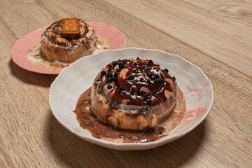 Two assorted cinnamon buns on plates ready to be eaten