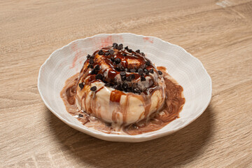 A delicious cinnamon roll with chocolate topping in a white bowl