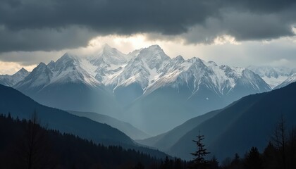 Majestic snow-capped mountain range under dramatic cloudscape. Layers of blue mist, dark forests create depth in valleys. Sunlight breaks through stormy grey clouds, illuminating rugged peaks in