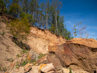 Large sandstone rock in foreground with eroded sandy hillside and trees in background under clear...