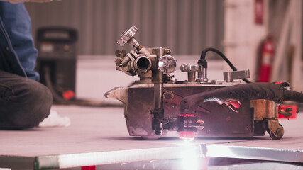 A technician operates welding machinery on a workbench in an industrial workshop. The environment...