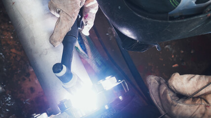 A skilled worker is focused on welding a metal pipe using a welding torch. The process emits a bright light, highlighting the precision and care required for the task