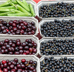 Fresh organic fruits and vegetables at local farmers market. Close-up of eco-friendly cardboard boxes filled with ripe cherries, black currants, and green peas in pods. Healthy natural food background