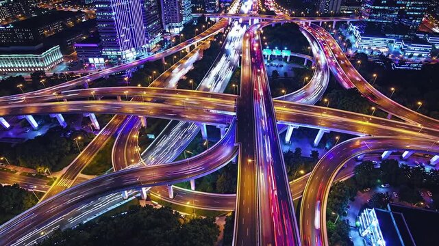 Highway interchange at night showing traffic flowing smoothly through a complex network of elevated roads and ramps, creating a mesmerizing pattern of light trails