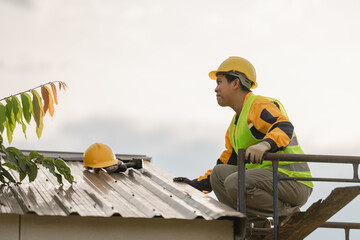 Worker in Construction Helmet Observing Roofing Project at Sunset, Safety Vest and Tools for Home...