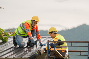 Two construction workers installing metal roofing on a building site, wearing safety gear and helmets, with mountains in the background under a cloudy sky © pichet