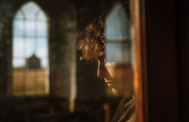Young man reflecting in abandoned church with sunlight streaming through window