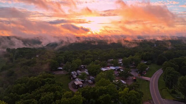 Low-hanging clouds sit on treetops at an RV park in Branson, Missouri in front of a beautiful sunset.