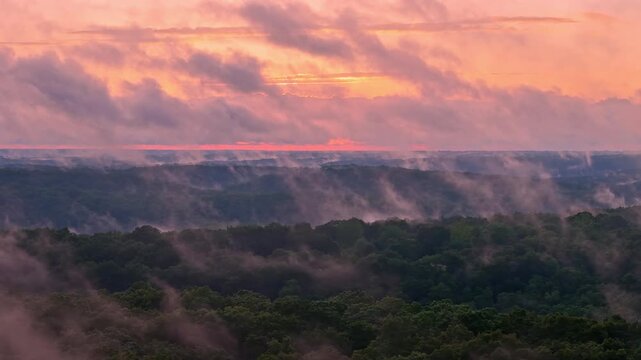 Scattered clouds slightly obscure a beautiful pink and orange sunset over the hills of Branson, Missouri.