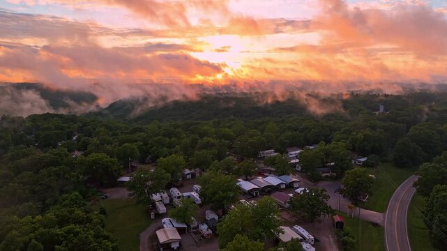 A bright sunset with orange and yellow colors is obscured by low-hanging clouds above an RV park in Branson, Missouri.