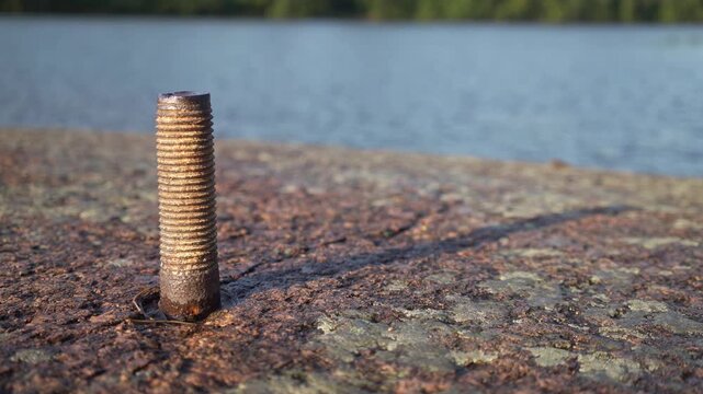 Rusty threaded rod fixed into rock by lakeside in Finland