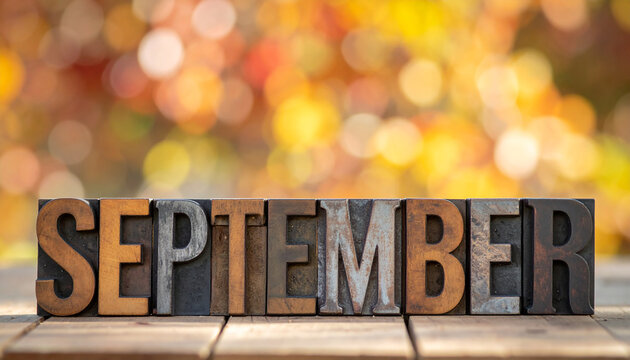 Text September made with mixed material letters. Wood, metal and stone. Rustic table. Soft bokeh