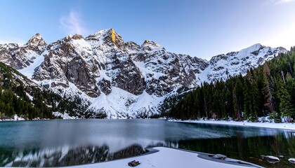 A serene winter landscape showcases a tranquil lake nestled amongst snow-capped mountains, reflecting the vibrant sky.