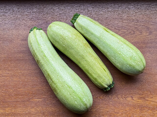 A bountiful harvest of zucchinis rests on a wooden windowsill near the window, showcasing fresh, ripe vegetables in natural light.