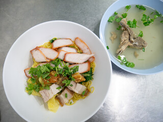Chinese egg noodles with roasted red pork, crispy pork belly, and wontons in a bowl on table.