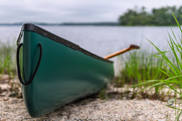 Green canoe resting on sandy lakeshore with paddle