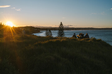 Obraz premium Friends enjoying scenic sunset overlooking ocean from grassy hilltop