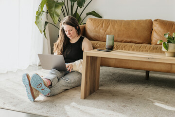 Middle aged woman sits on floor while working on laptop computer