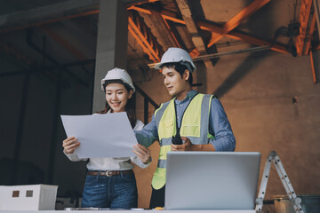 Construction manager and engineer dressed in orange work vests and hard helmets explore...