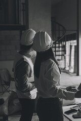 Construction manager and engineer dressed in orange work vests and hard helmets explore construction documentation on the building site near the steel frames