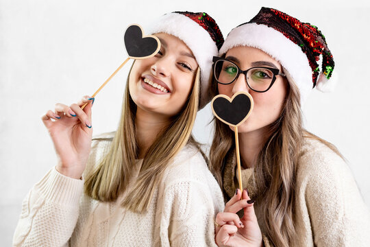Two happy girls wearing Santa hats holding Christmas props against white background