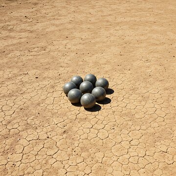 polished boules resting on a fine gravel court, the morning sun casting long, sharp shadows across the pebbles, with a solitary cochonnet slightly off-center