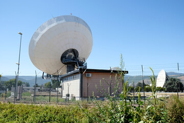 A large cluster of satellite dishes and antennas at the Fucino Space Centre, with a clear blue sky...