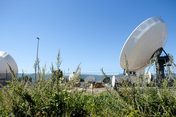 A large cluster of satellite dishes and antennas at the Fucino Space Centre, with a clear blue sky...