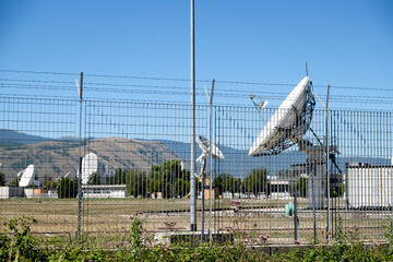 A large cluster of satellite dishes and antennas at the Fucino Space Centre, with a clear blue sky...