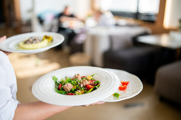 Waiter serving three plated meals in a restaurant. Colorful salad, mushroom dish, and garnish...