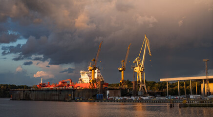 Obraz premium Beautiful storm clouds illuminated by the setting sun over the shipyard in Szczecin, Poland