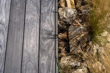 Gros plan sur des lames de parquet de terrasse grises avec délimitation de la pelouse réalisée en gros cailloux décoratifs.