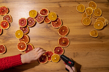 DIY process of Woman using hot glue Christmas arrangement with dried oranges and grapefruits....