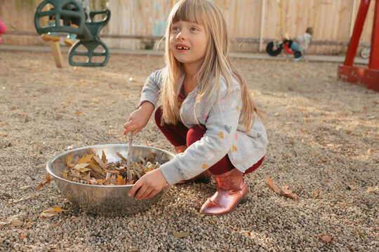 Preschool girl gathering autumn leaves on playground