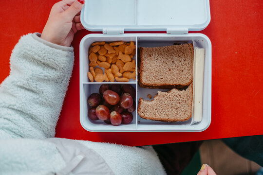 Child opening lunchbox with sandwich, grapes, and crackers