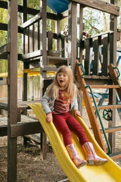 Preschool girl enjoying slide at playground in autumn
