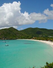Serene bay with turquoise water, white sand, and lush green hills under a partly cloudy sky