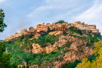 Obraz premium beautiful highland landscape of old town on a top of amazing mountain with green slopes and trees on foreground and amazing blue cloudy sky on background
