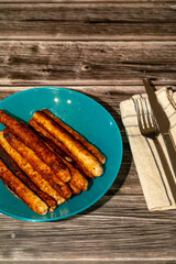 A blue plate of sausages with a napkin, knife and fork on a wooden table