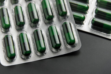 Foil blister pack of pharmaceutical natural herbal green capsules on black ceramic background....