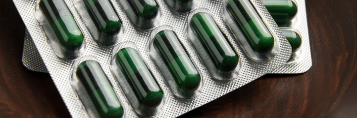 Green medicinal herbal capsules in blister pack in wooden container close up