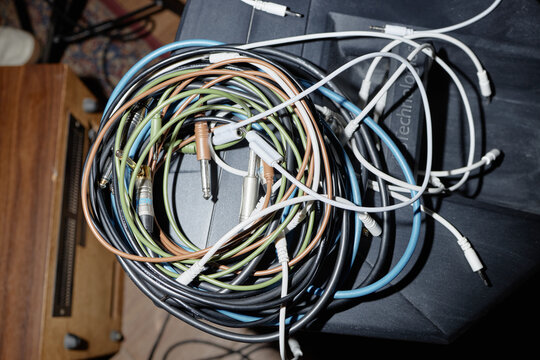 Closeup showing tangled bundle of various audio cables and connectors resting on dark surface, including multiple quarter inch and mini jack plugs, emphasizing electronic equipment setup