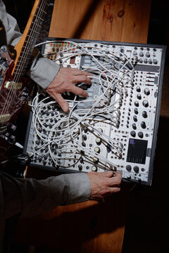 Caucasian man adjusting modular synthesizer cables and controls, playing electric guitar, focusing on electronic music production, hands visible manipulating equipment