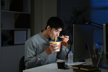 Asian young businessman eating noodles while working in office at night.